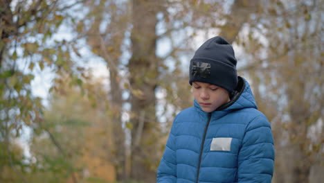 niño caminando a lo largo de los árboles secos pensativo, da la vuelta a su bolsa al revés y vierte hojas secas en el suelo, rodeado de vibrantes hojas de otoño y la naturaleza