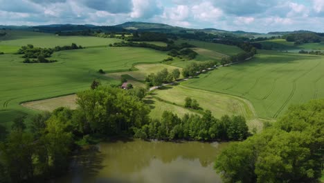 Aerial-view-of-a-placid-green-ladscape-with-fields,-green-vegetation-and-a-pond