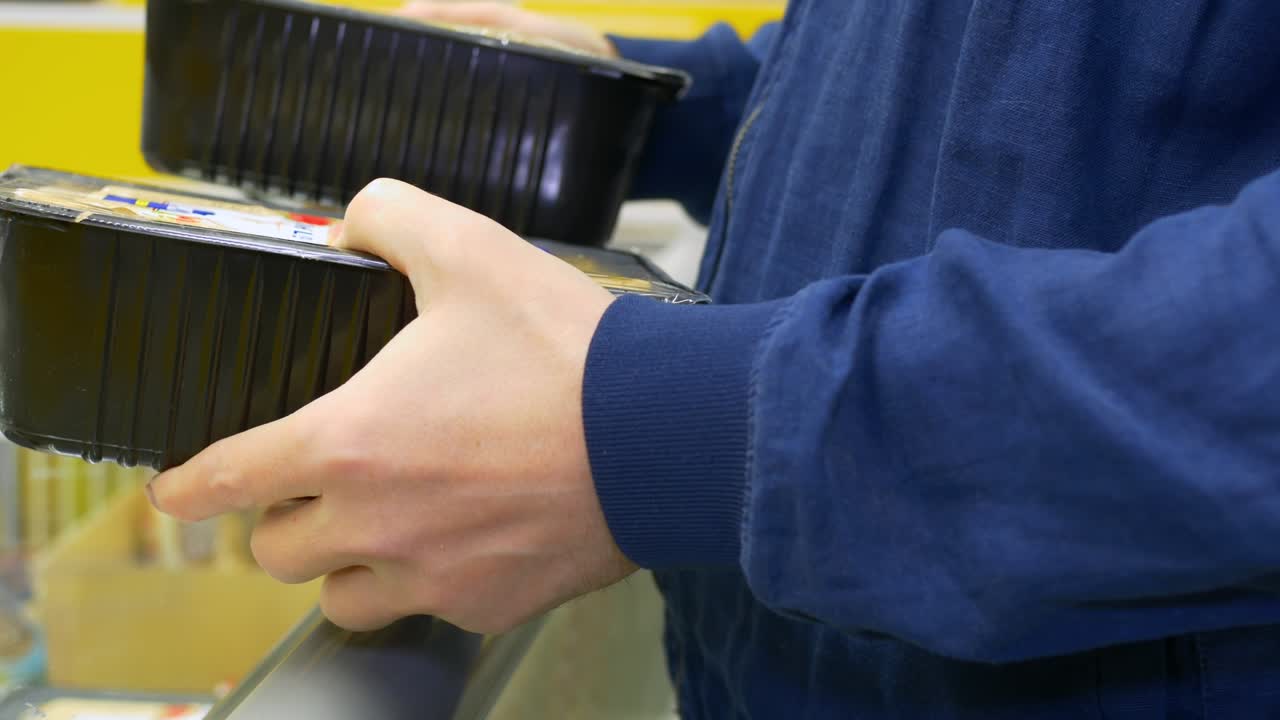 상점에 있는 한 남자가 냉동식품을 선택하고, 냉장고 선반에서 두 개의 식품 패키지를 꺼내서 조성을 읽고, 하나를 선택하고, 식료품을 지불하기 위해 체크아웃으로 간다.