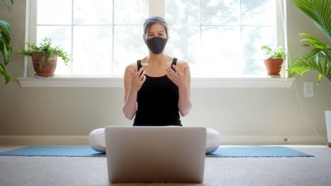 young woman sitting and chatting remotely on her laptop while wearing a medical face mask