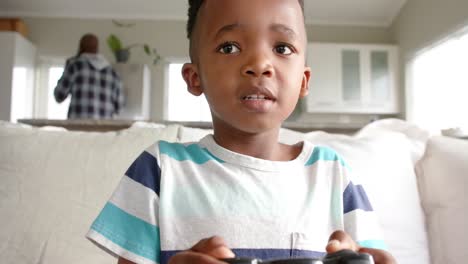 happy african american boy sitting on sofa and playing video games, slow motion