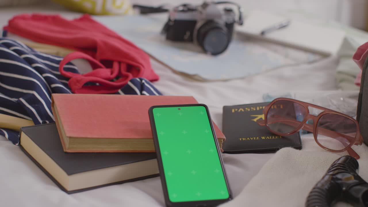 teléfono móvil de pantalla verde con maleta abierta en la cama en casa siendo empacado para las vacaciones de verano 1