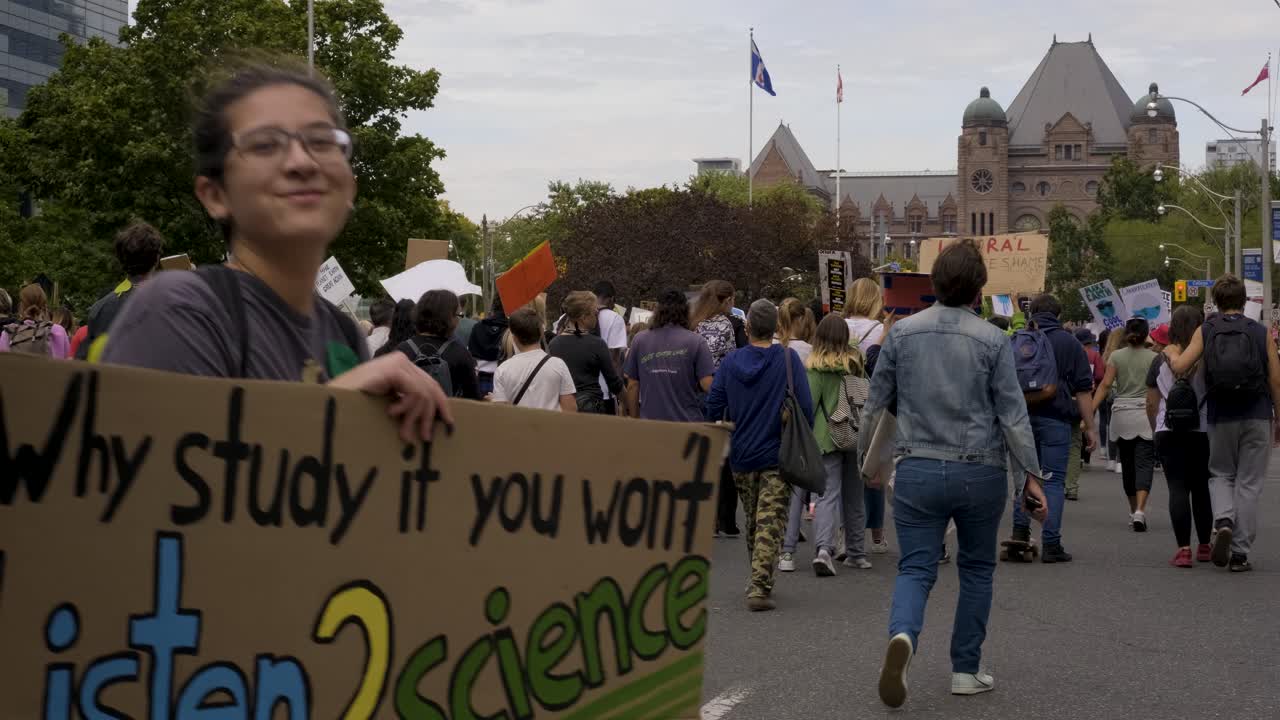 Queen’s Park, Toronto, Canada - A young woman happily showing her slogan with the rest of the crowd going for the Climate Change Campaign -  wide shot