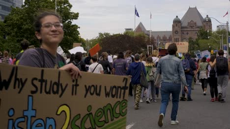 queen’s park, toronto, canada - a young woman happily showing her slogan with the rest of the crowd going for the climate change campaign -  wide shot