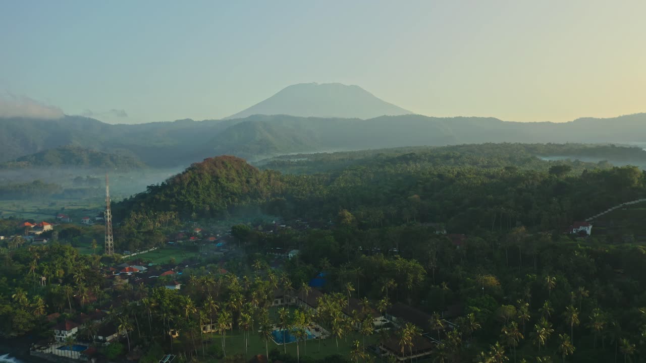 Spettacolare veduta aerea del Monte Agung a Bali all'alba, che mostra foreste lussureggianti, pendii vulcanici e l'oceano blu profondo in un drammatico paesaggio tropicale.