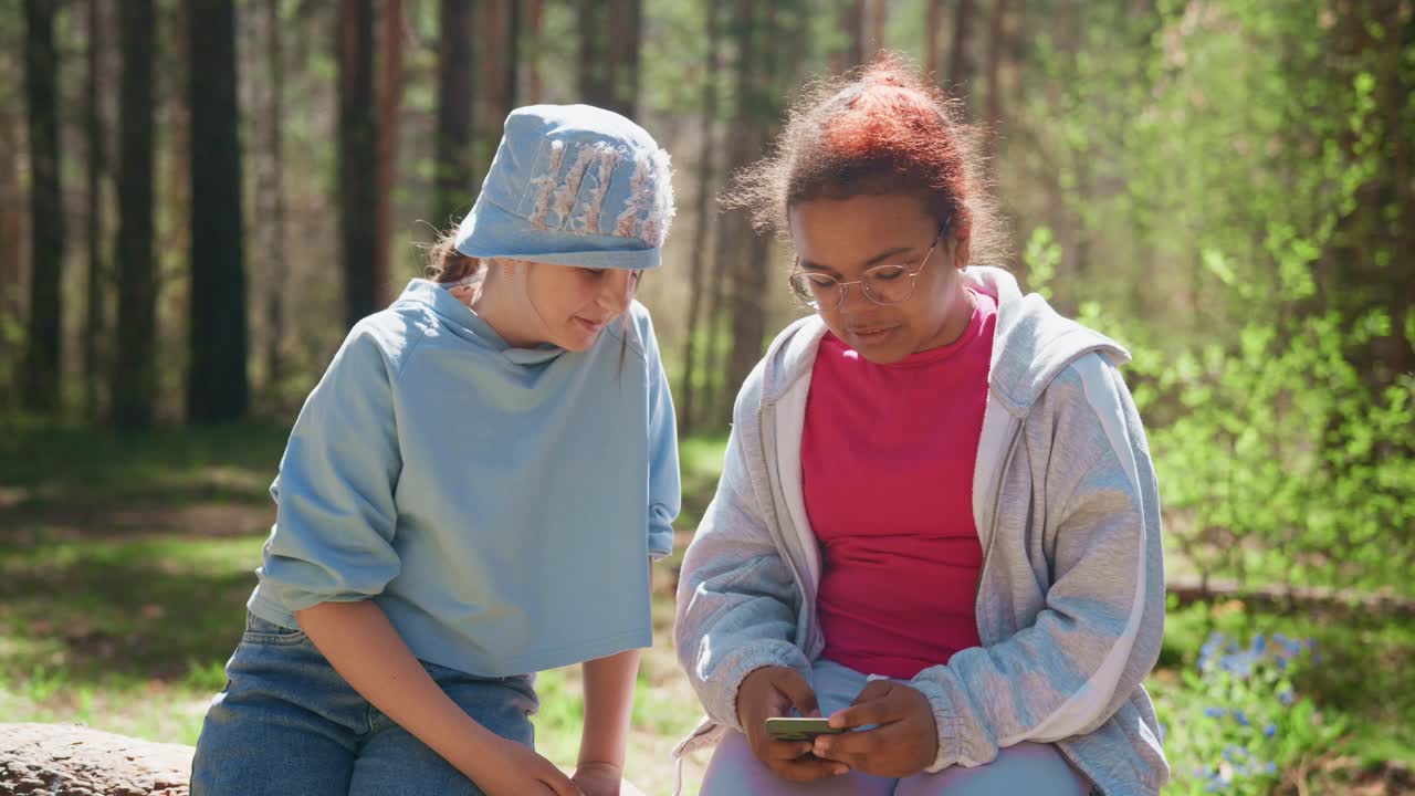 Two girls using a phone in a forest