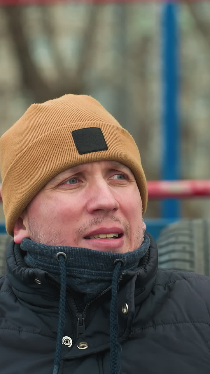 A coach seated on workout equipment appears contemplative, in the background, two boys play football