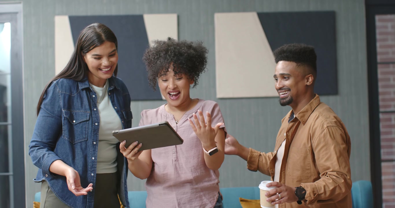 Diverse coworkers gathering in office lounge center woman showing tablet, team smiling at news
