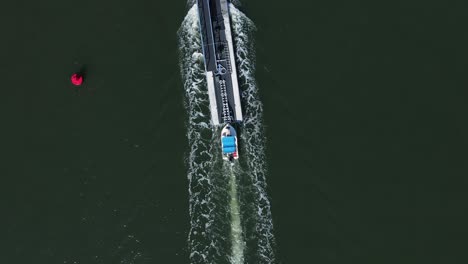 Ein-Kleines-Boot,-Das-Einen-Großen-Ponton-Liefert,-Passiert-Eine-Navigationsmarkierung-Auf-Einem-Flusskanal