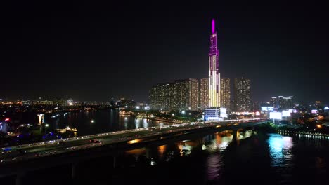 dolly aéreo a la derecha con el tráfico acelerando rápidamente sobre el puente y el moderno horizonte alto en el fondo por la noche en la ciudad de ho chi minh, vietnam