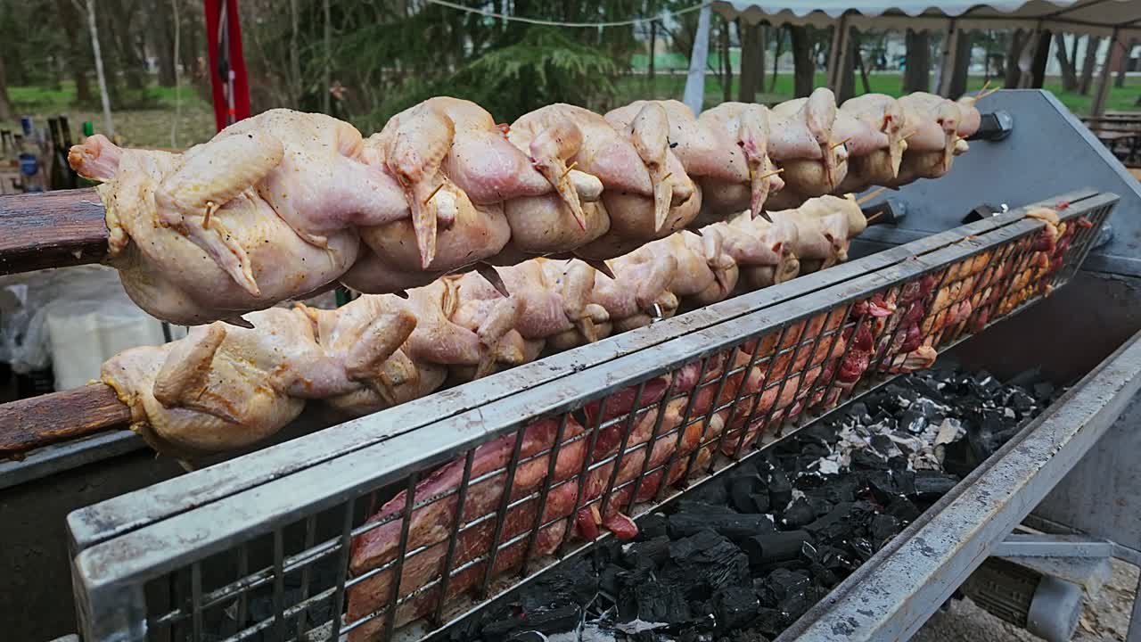 Roasting trussed chickens and pork meats on festival BBQ rotisserie