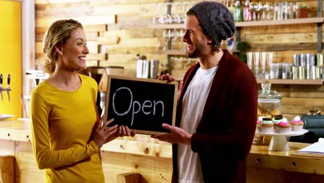 Owners-standing-with-open-sign-board-in-cafe