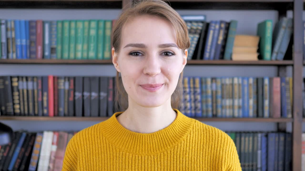 Pollice in su di una giovane donna al lavoro, che guarda la telecamera.
