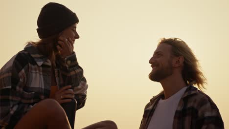 Ein-Blondes-Mädchen-Mit-Schwarzem-Hut-Und-Kariertem-Hemd-Gibt-Ihrem-Freund-Bei-Sonnenaufgang-In-Der-Nähe-Des-Meeres-Eine-Tasse-Heißen-Tee-Aus-Einer-Thermoskanne