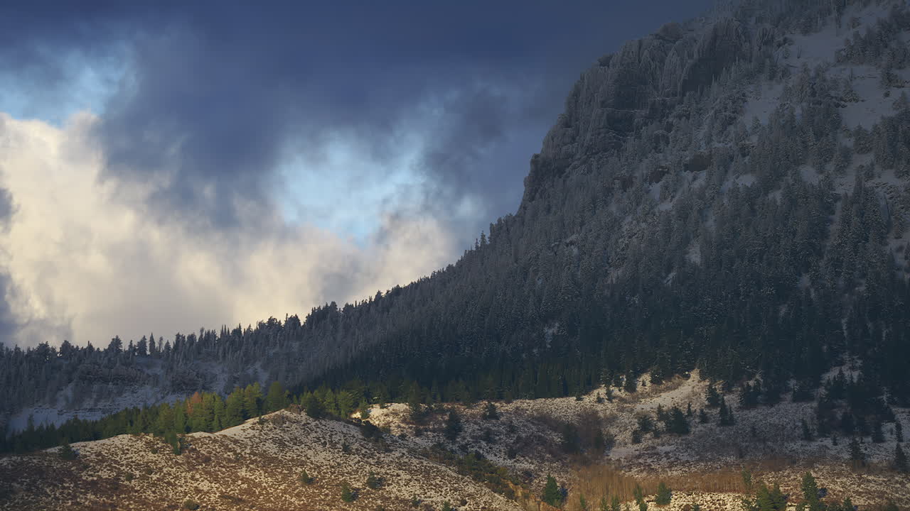 montaña densamente boscosa cubierta de nieve contra el cielo nublado al atardecer
