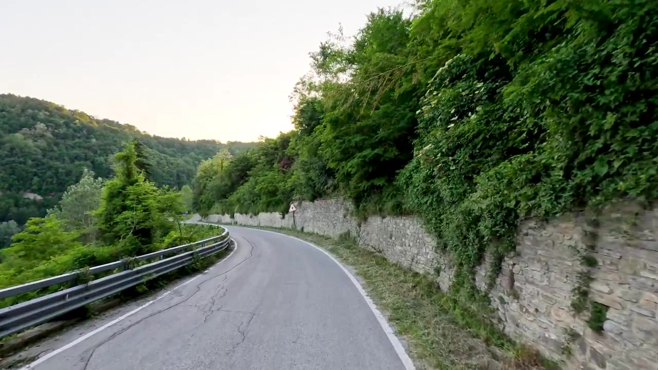 Prospettiva in prima persona mentre si guida lungo una strada di montagna panoramica con muri in pietra durante l'ora d'oro.