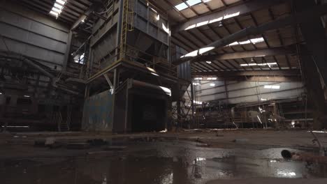 slider footage of machinery in an abandoned brick factory with a wet floor in the foreground, shale storage, conveyor belts