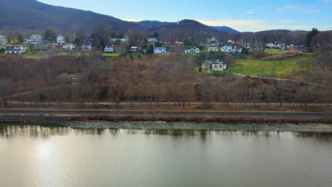 drone flying sideways past a small, picturesque village in new york on the banks of a river with a mountain backdrop