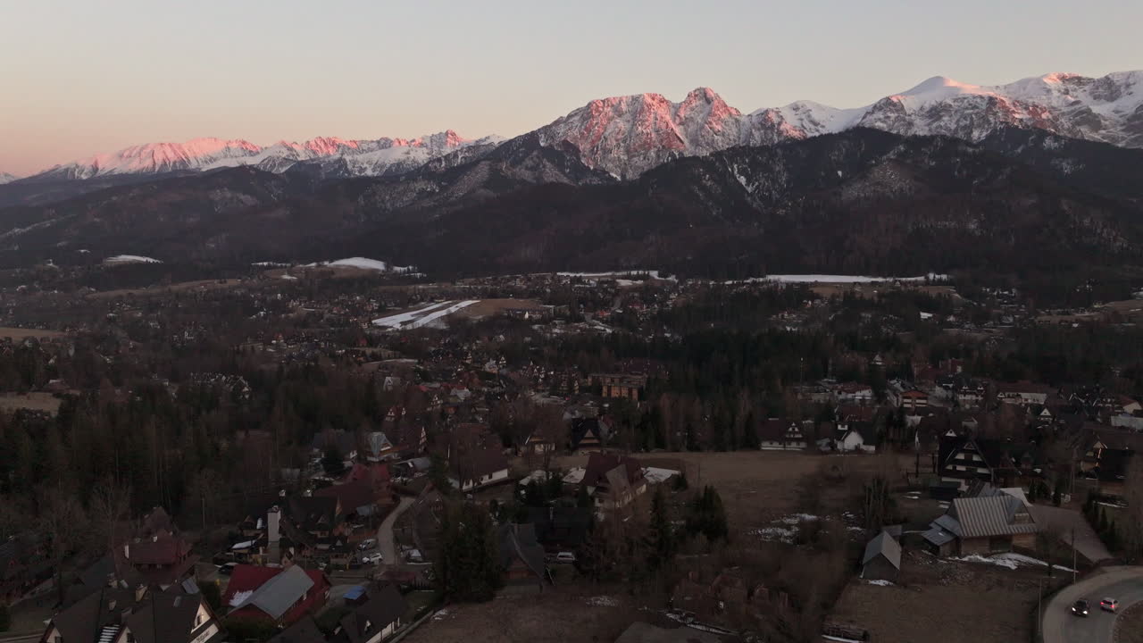 Reveal drone shot of Tatra Mountains with snow and Zakopane cityscape at sunrise in Podhale region, Poland