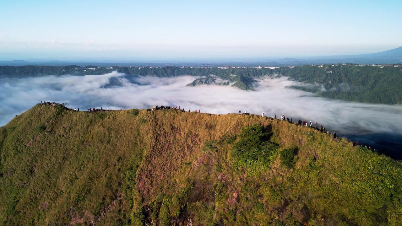 Escursionisti su stretta cresta di montagna sopra un mare di nuvole, con ripido terreno vulcanico e viste panoramiche su una valle verde, creando un drammatico paesaggio ad alta quota, filmato aereo con drone in avvicinamento.