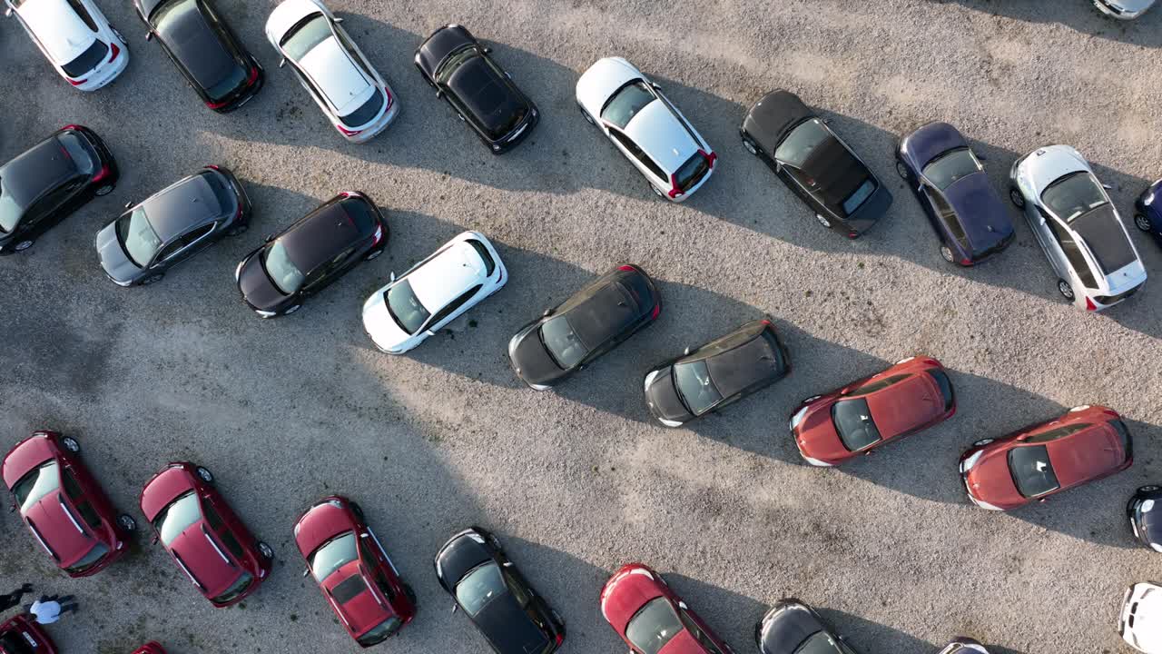 Aerial view of many colorful cars parked on parking lot with lines and markings for parking places and directions