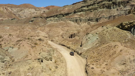 dark black suv sits parked on the side of a curved dirt road through the rainbow basin in the mojave desert