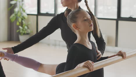 profesora corrige la posición de las piernas de la chica gimnástica en la clase de ballet