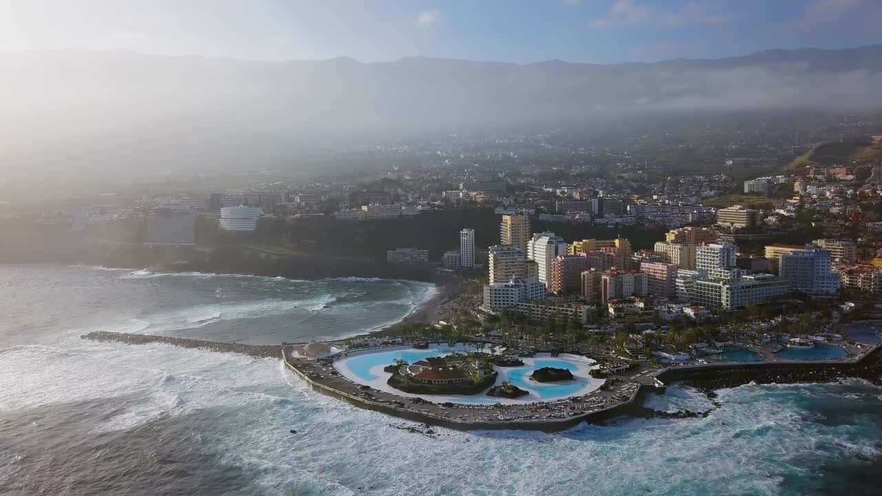 푸에르토 데 라 크루즈의 공중 파노라마 - 바다의 파도에 둘러싸인 리조트와 수영장, 테네리페, 카나리아 제도, 스페인
