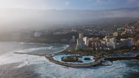 panorama aéreo de puerto de la cruz resorts y piscinas rodeados de olas marinas, tenerife, islas canarias, españa.