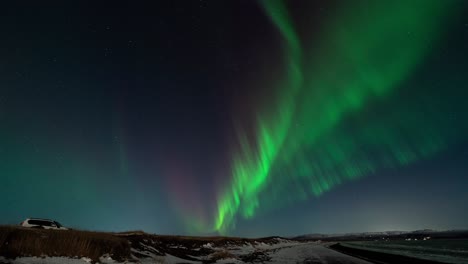 Time-lapse-shot-of-flickering-green-and-purple-lights-at-sky-over-snowy-Iceland-in-winter---wide-shot