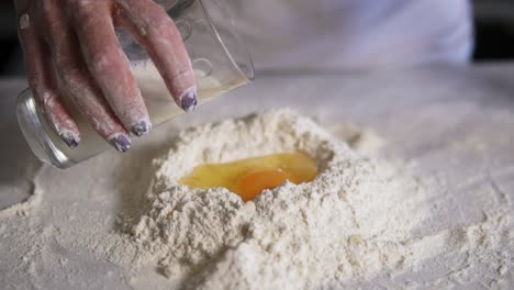 close up view of female hands adding milk from the glass to the flour with eggs on the kitchen table. slow motion shot