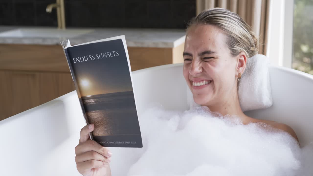 Женщина берет книгу "ENDLESS SUNSETS", лежа в ванне с пеной и белой подушкой, расслабляется и читает.