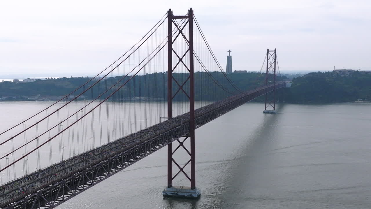 Beautiful aerial drone shot of thousands of long distance half marathon and 10k runners crossing the 25th April bridge in Lisbon, Portugal during a road race. Sports, health, wellbeing and fitness