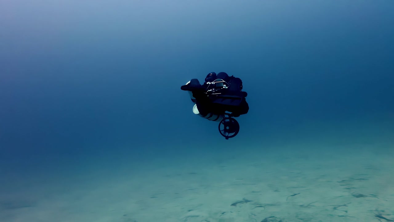 Underwater technical diver exploring deep blue Mediterranean sea of Malta Gozo Comino during sunny summer season using DPV scooter filmed with wide angle front view featuring turquoise sand bottom