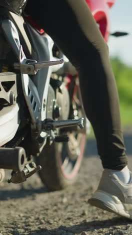 primer plano de un motociclista arrancando su motocicleta en la carretera, con un coche en la distancia acercándose en la dirección opuesta