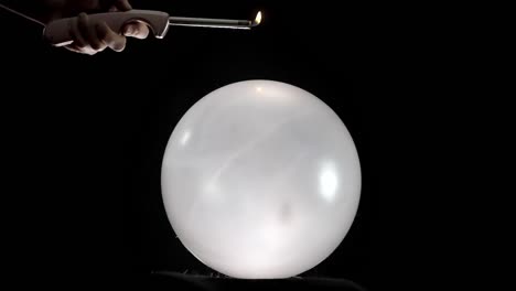 a dramatic scene where a big round white balloon pops as a hand holding a lighter approaches it. the tension builds as the flame nears, culminating in the sudden burst of the balloon.