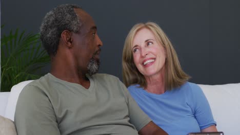 mixed race senior couple using digital tablet while sitting on the couch at home