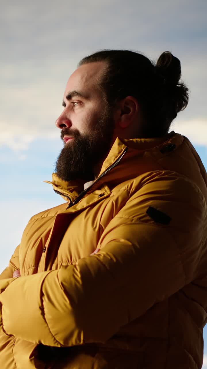 Uomo barbuto pensieroso in piumino giallo che guarda il cielo
