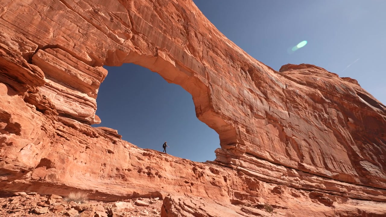 Donna con zaino che cammina sotto il suggestivo Arco Jeep, monumento naturale di Moab, Utah, USA