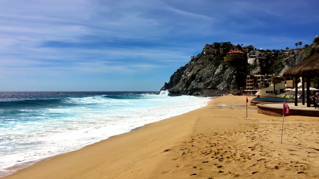 Ondas fortes quebrando em uma praia ensolarada com uma falésia ao fundo