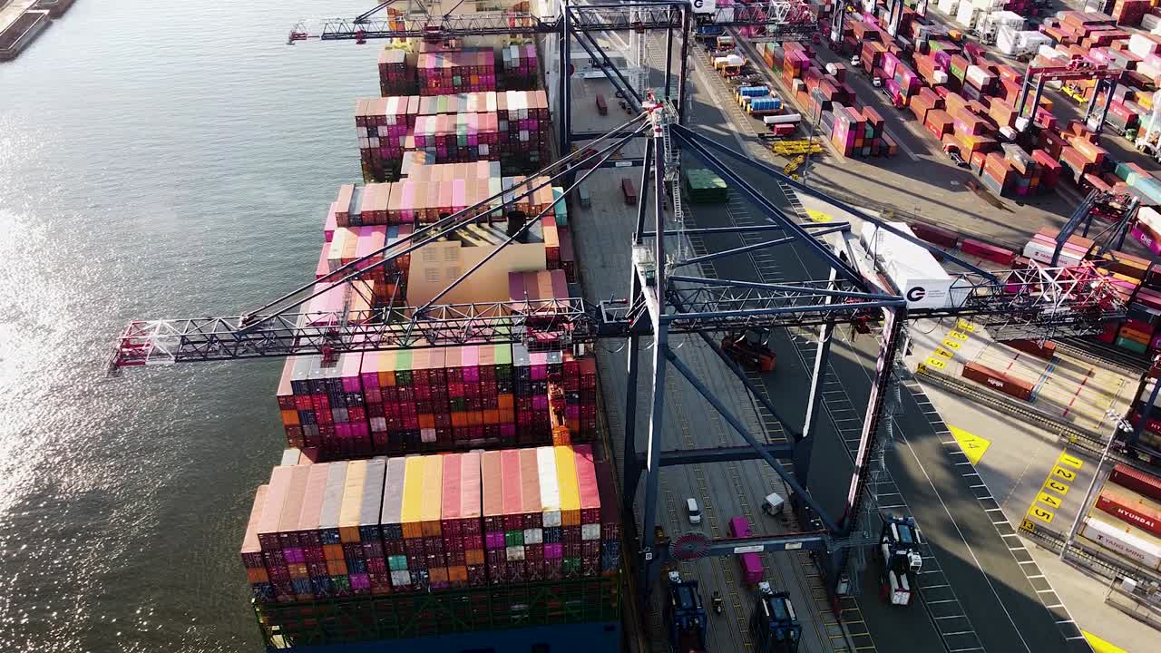 Cargo ship being loading with shipping containers while docked at port near New York City - Aerial footage from behind
