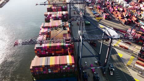 cargo ship being loading with shipping containers while docked at port near new york city - aerial footage from behind