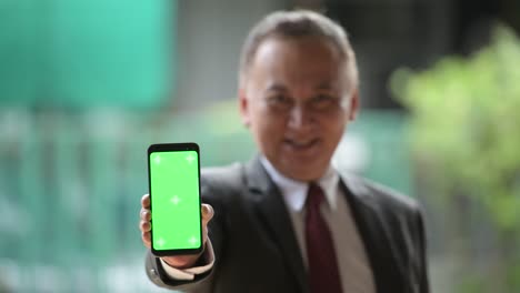mature japanese businessman showing phone in the streets outdoors