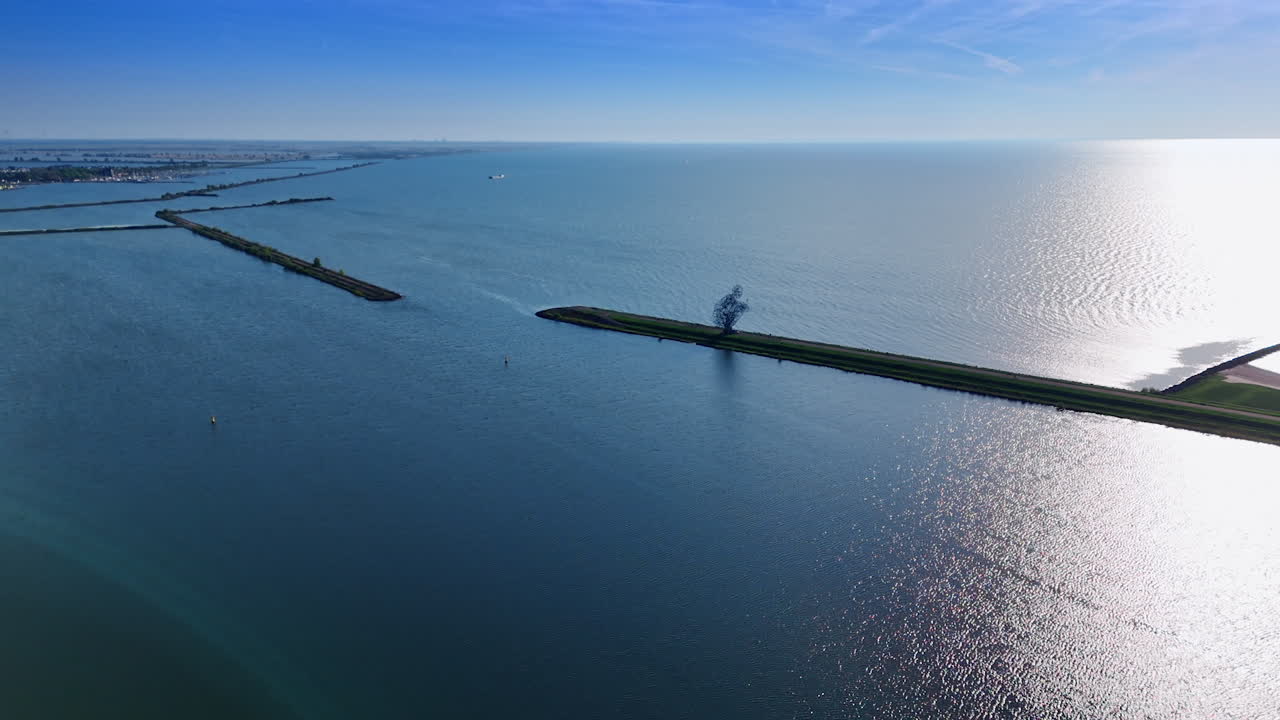 Dams on the waterscape of Markermeer Lake sparkling in the sun. Approaching the iron figure of man sitting over the water. Lelystad, the Netherlands.