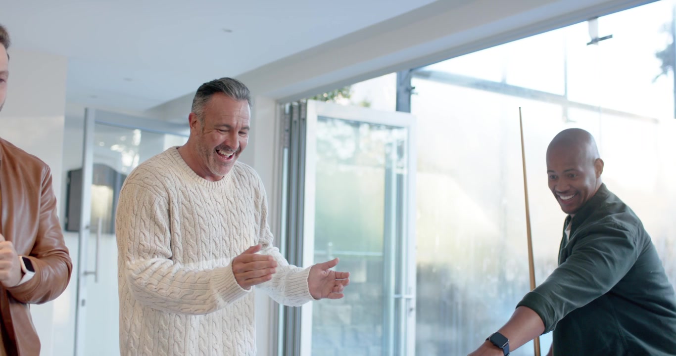 Diverse male friends cheering African American man lining up, striking cue at home, sinking balls