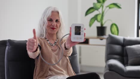 elderly woman giving thumbs up while holding blood pressure monitor