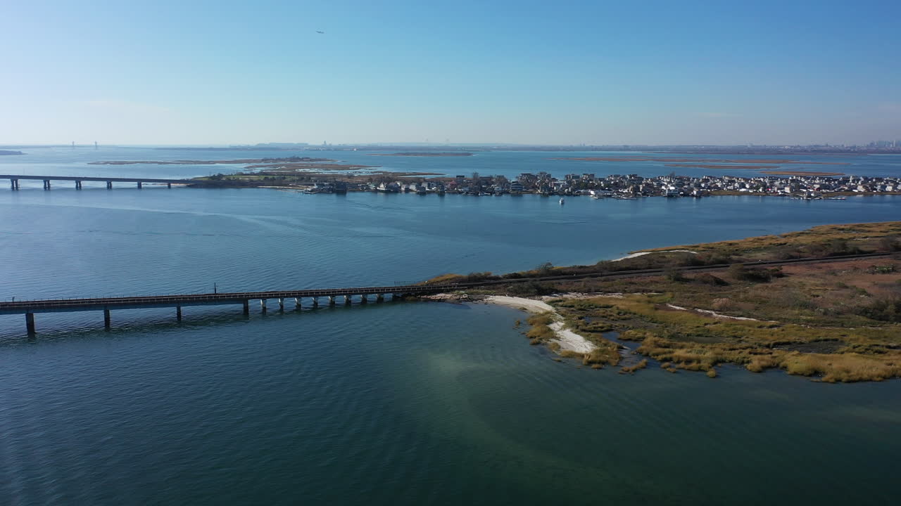 una toma aérea de vías de tren elevadas con un puente colgante sobre una bahía en queens, nueva york