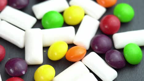 sweets colored candies skittles and mint chewing pads, colored sweets rotate on a black plate