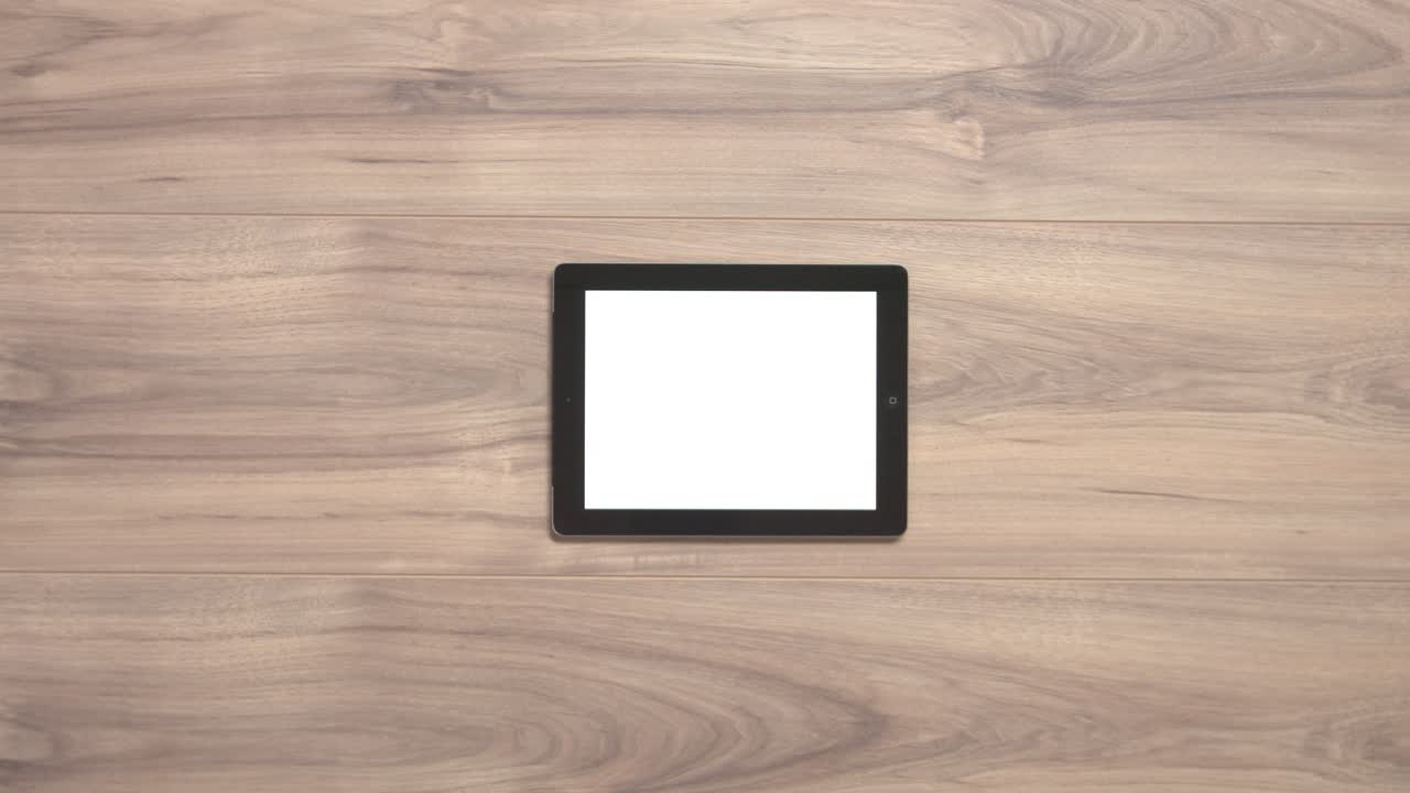 Two hands pulling a tablet with a white screen away from a wooden table