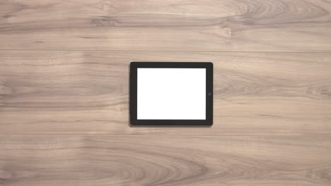 Two-hands-pulling-a-tablet-with-a-white-screen-away-from-a-wooden-table